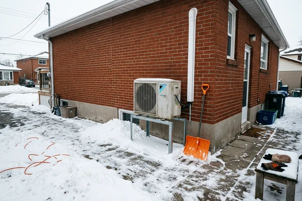 Cold-climate heat pump outdoor unit on a raised snow stand beside a detached home