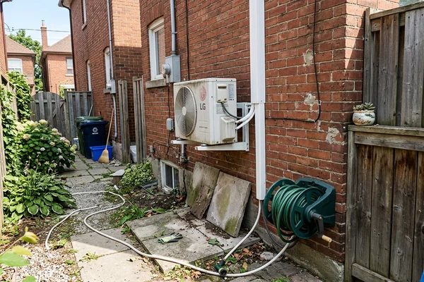 Compact mini-split condenser on wall brackets in a narrow Toronto side yard