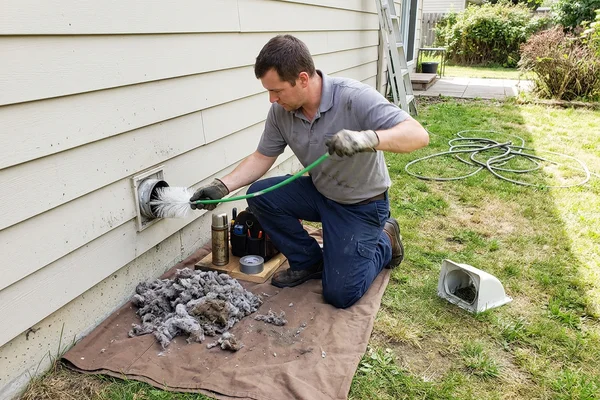 Technician clearing lint from a dryer vent at an exterior wall termination