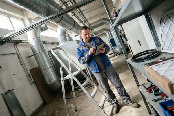 Technician recording maintenance readings on a tablet in a warehouse mechanical room