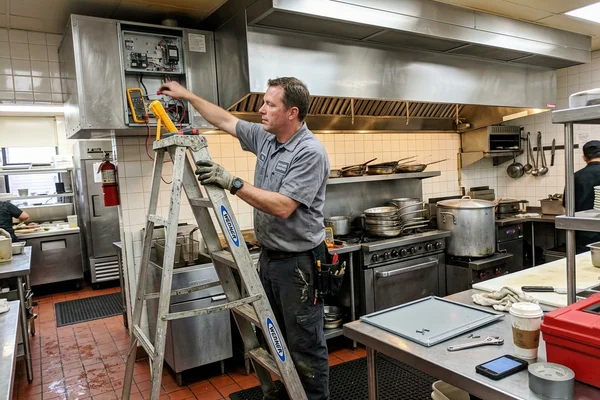 Technician servicing a commercial kitchen make-up air unit beside an exhaust hood